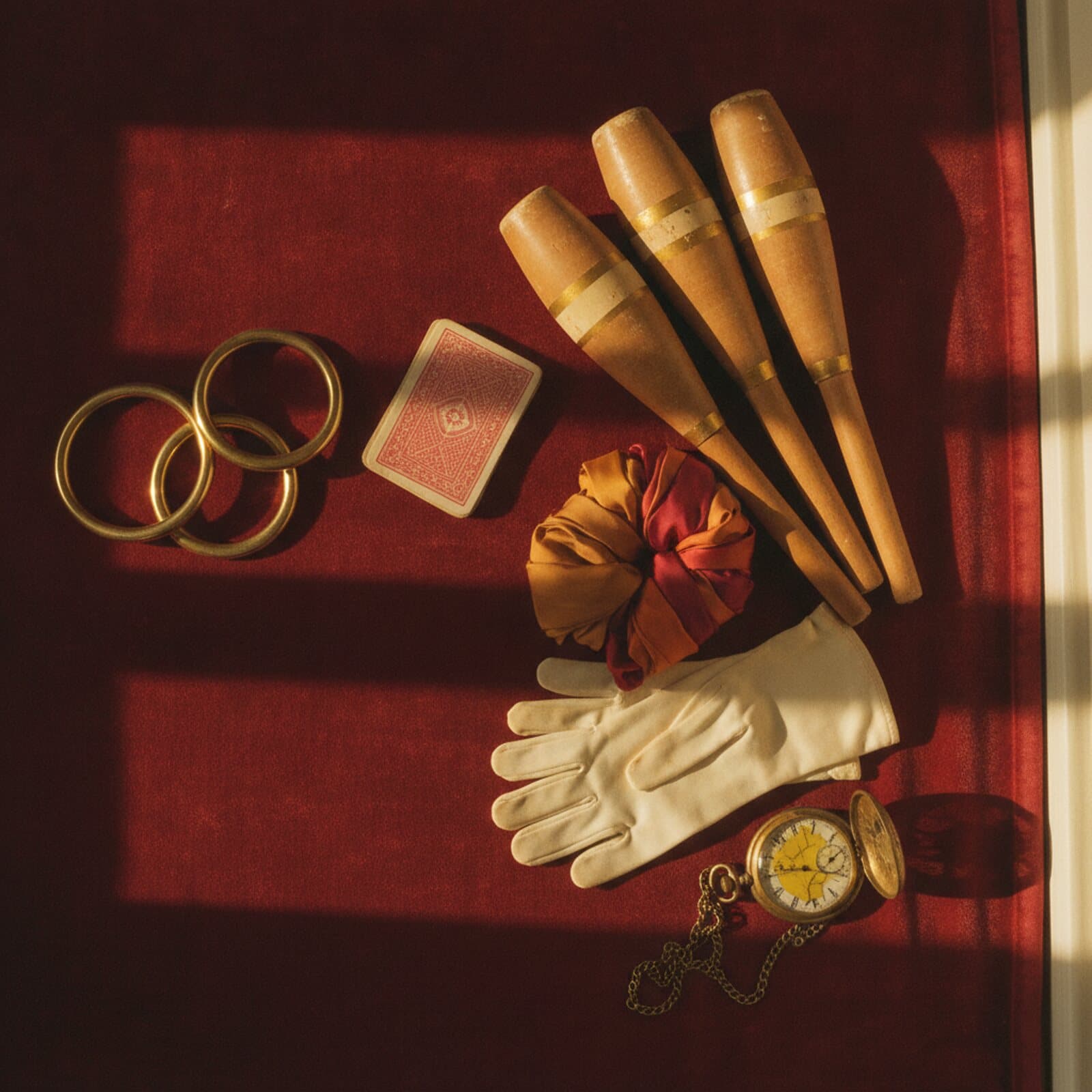Messingringe, ein Kartenspiel, drei Keulen, Seidentücher, weiße Handschuhe und eine Taschenuhr auf bordeauxrotem Samt